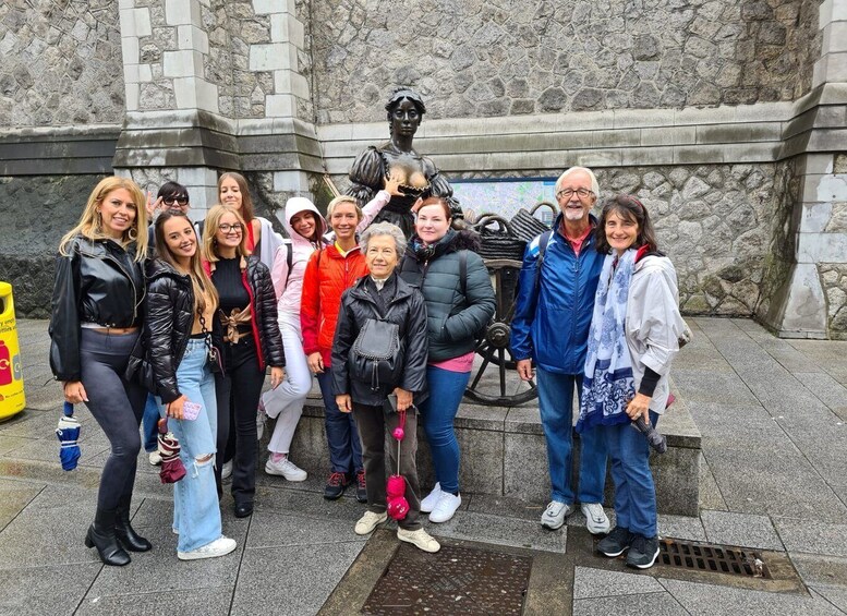 A group of people standing in front of a statue and a stone wall. 5