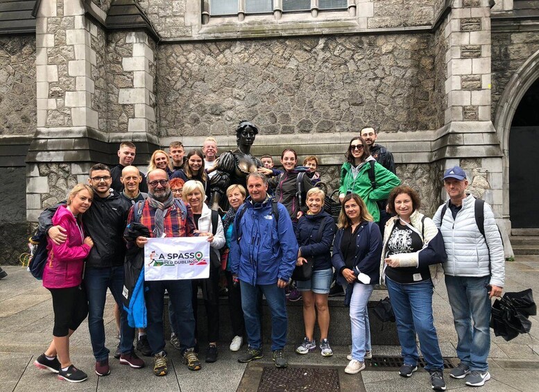 A group of people standing in front of a stone building with a statue. 1