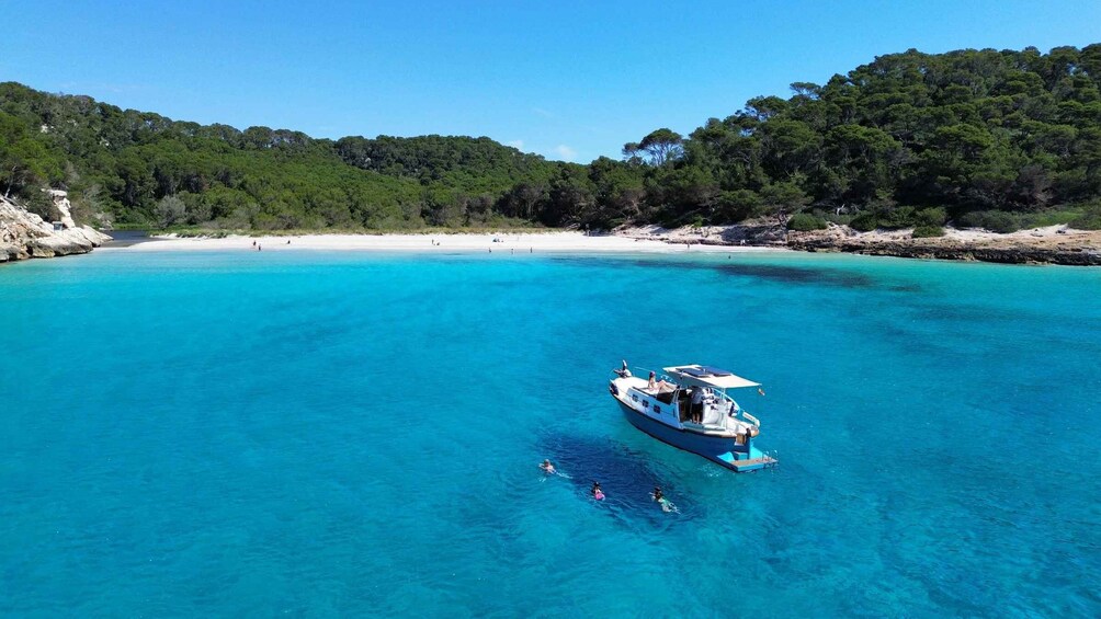 A boat on clear turquoise waters with a beach and forested hills in the background. 3