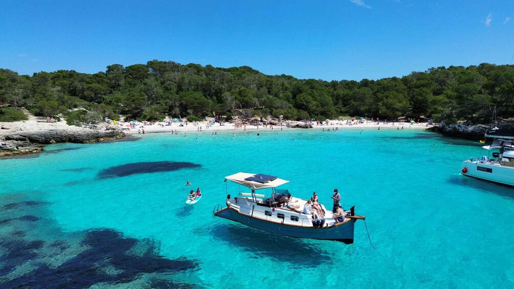 A boat anchored in turquoise waters with a beach and forested area in the background. 2