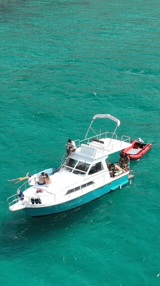 A white boat with a red dinghy docked alongside it, both on turquoise water. 1