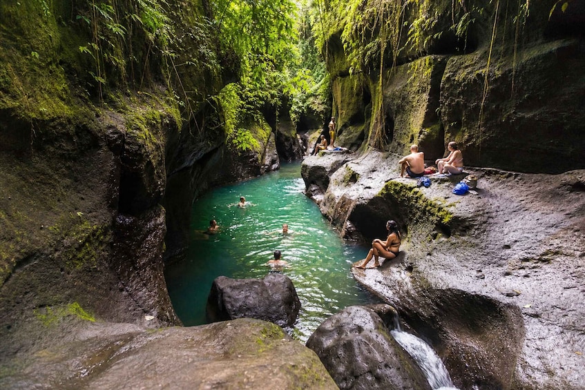 Un'area naturale con acqua circondata da rocce e vegetazione, dove persone nuotano e si rilassano sulle pietre. 2