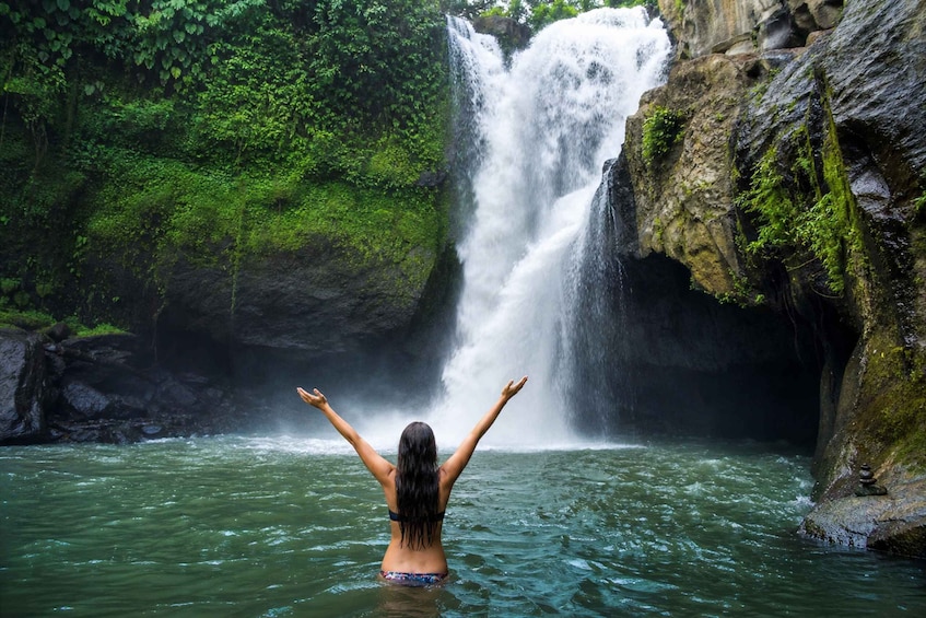 Una cascata in una zona boschiva, con una persona in acqua che guarda la cascata. 1