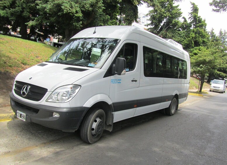 A white Mercedes-Benz Sprinter van parked on a street with trees and a grassy hill in the background. 3