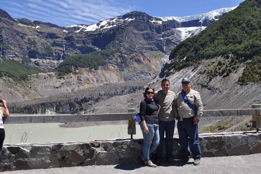 A group of people standing on a stone bridge overlooking a glacier and mountains. 5