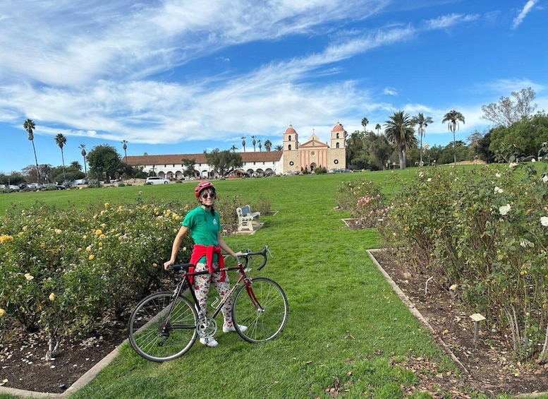 A person on a bicycle in a garden with a historic building in the background. 1