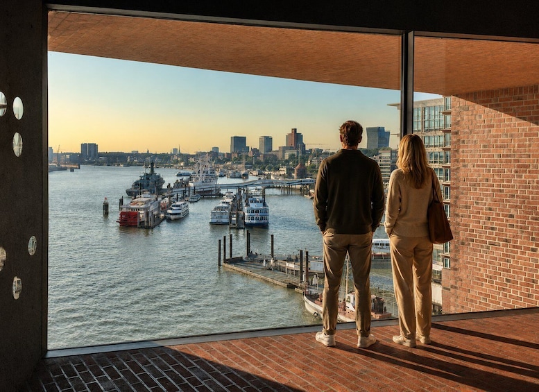 Two people standing on a balcony overlooking a harbor with boats and a city skyline. 2
