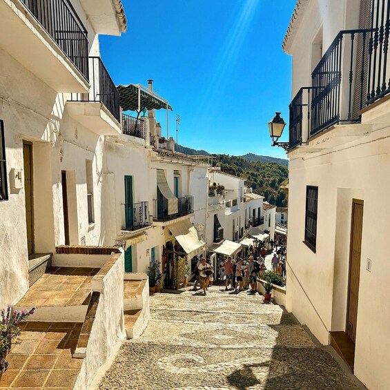 Una estrecha calle empedrada bordeada de edificios blancos con balcones, que conduce a una ladera. 2