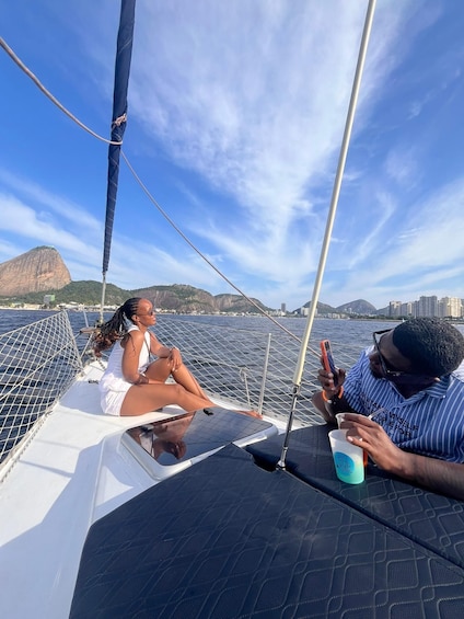Two people on a sailboat with a cityscape and mountains in the background. 3