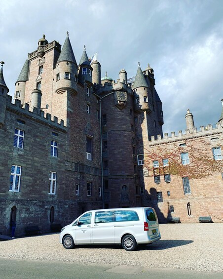 Un castillo con múltiples torres y un coche blanco estacionado al frente. 5