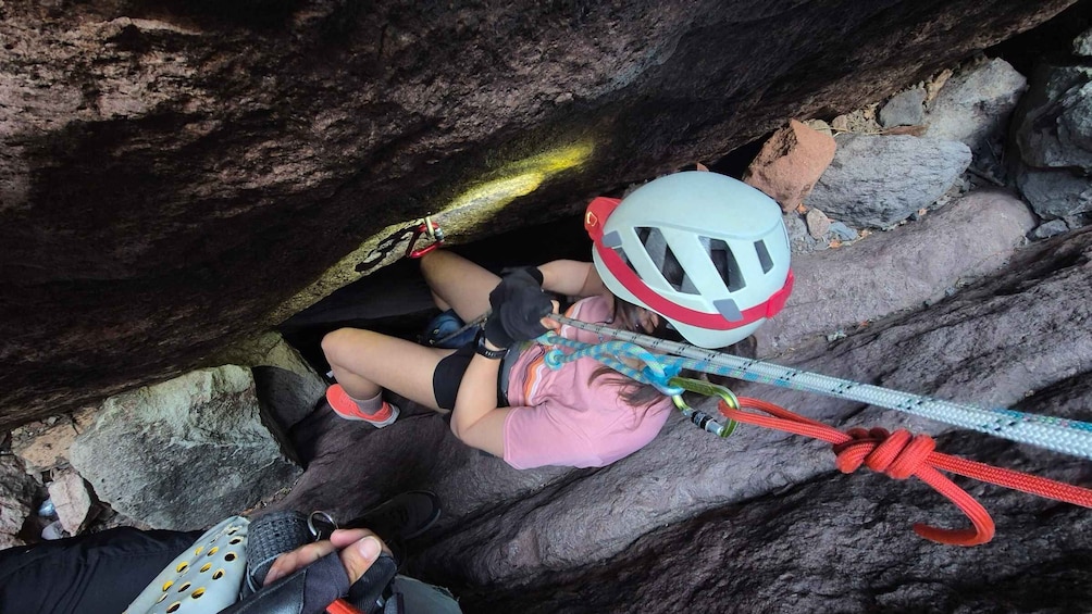 A person rappelling down a rocky cliff with a helmet and harness. 2