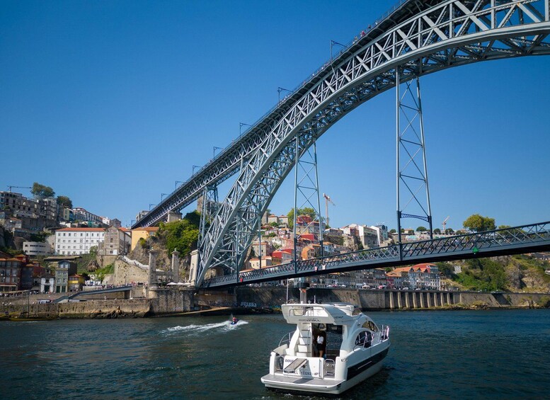 A boat on a river under a large steel bridge with a cityscape in the background. 5