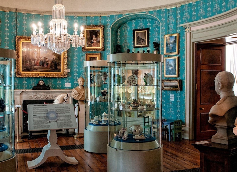 A museum interior with teal wallpaper, a chandelier, busts, and glass display cases. 3