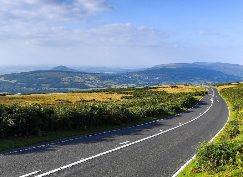 A curving road through a hilly landscape with fields and distant mountains. 5