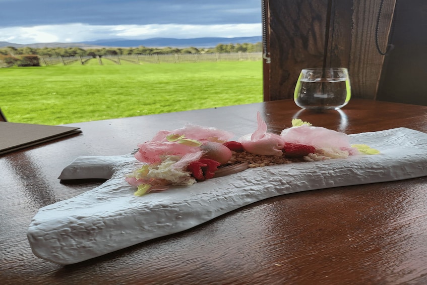 Een dessert op een houten tafel, met een mooi uitzicht op een groen veld en bergen op de achtergrond. 2
