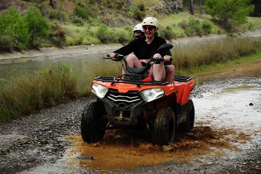 To personer på en ATV på en mudret sti nær vand. 2