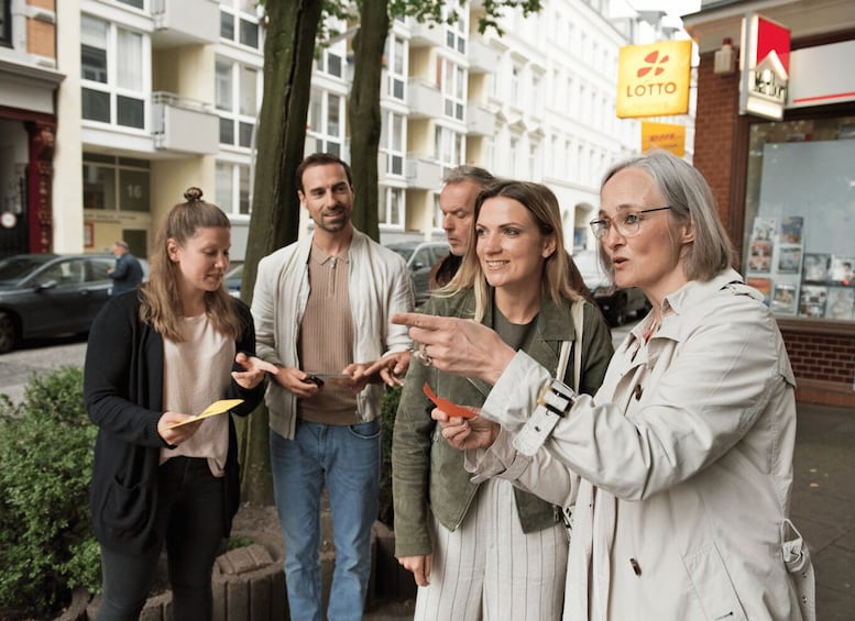Un grupo de personas de pie en una acera, con un edificio y un cartel que dice 'LOTTO' al fondo. 2
