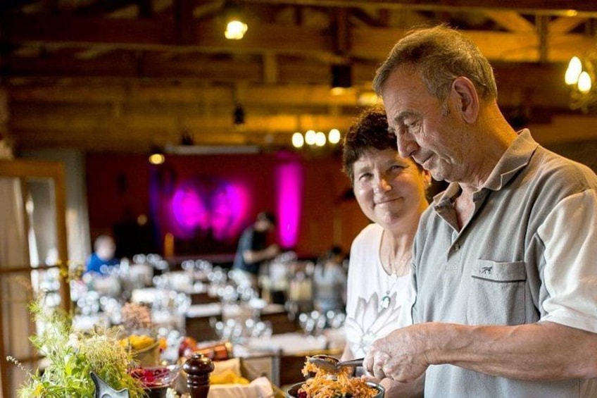A man and a woman at a buffet table with various dishes and a purple-lit background. 2