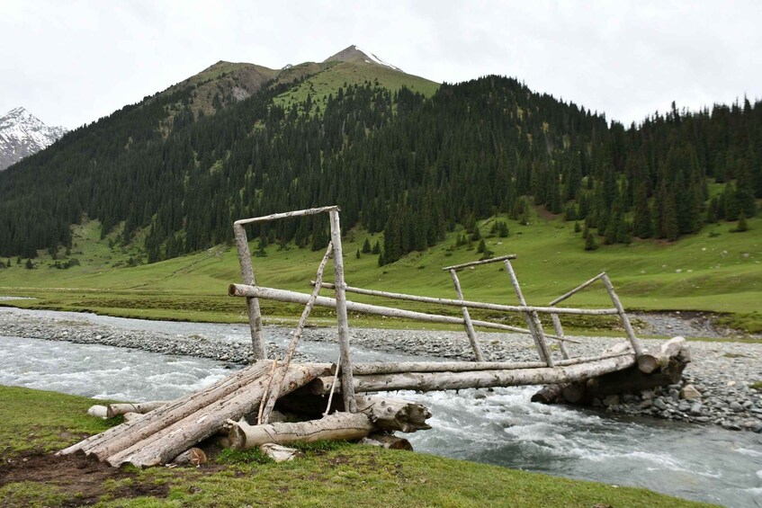 Un fiume con un ponte di legno in un paesaggio montuoso. 1