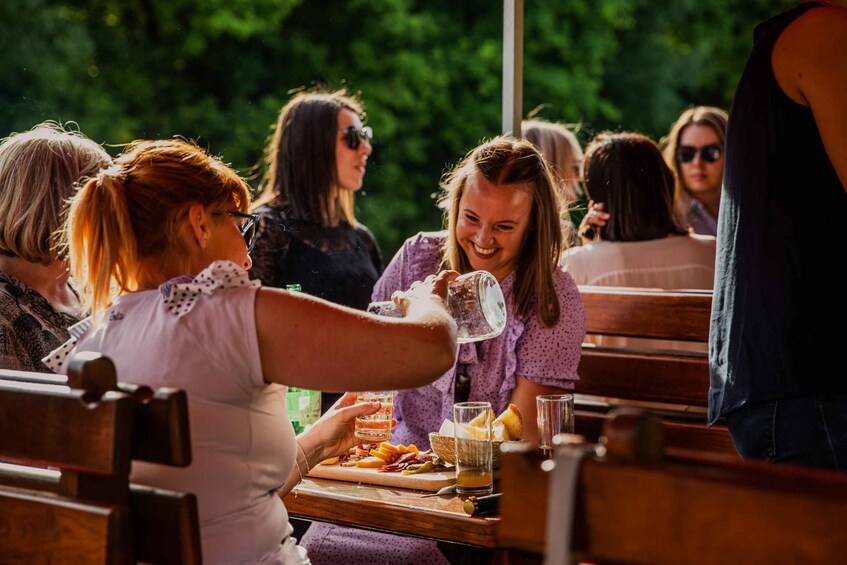 A group of people sitting at a wooden table outdoors, enjoying a meal with various cheeses and bread. 3