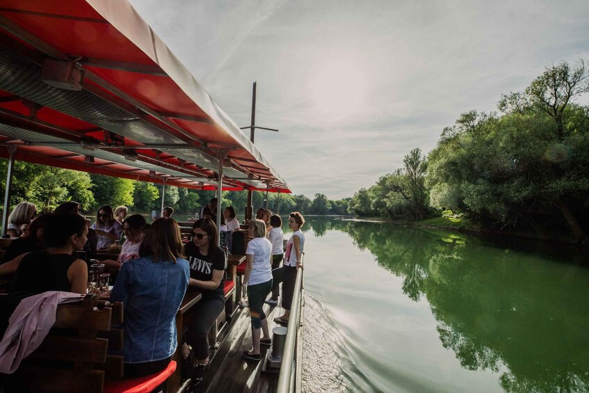 A group of people dining on a boat with a river and greenery in the background. 2