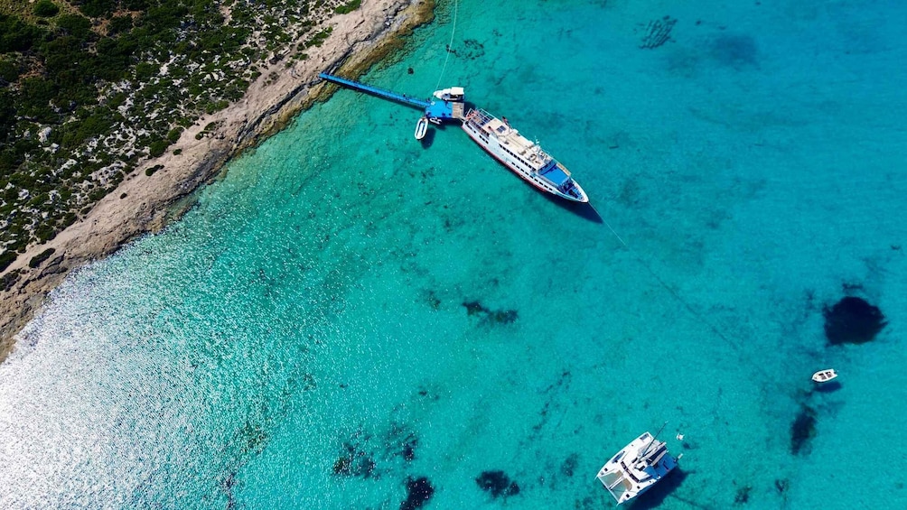 Vista aerea di una zona costiera con acque cristalline color turchese, una grande nave da crociera ormeggiata al molo e una barca più piccola nelle vicinanze. 2