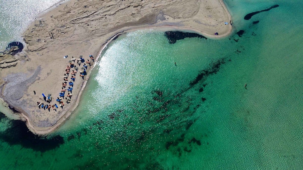 Vista aerea di una spiaggia con acque turchesi cristalline e un gruppo di persone riunite sulla sabbia. 3