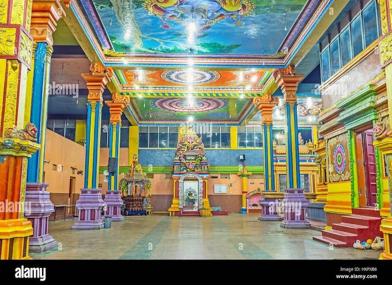 A brightly colored temple interior with ornate pillars, a central shrine, and a mural on the ceiling. 2