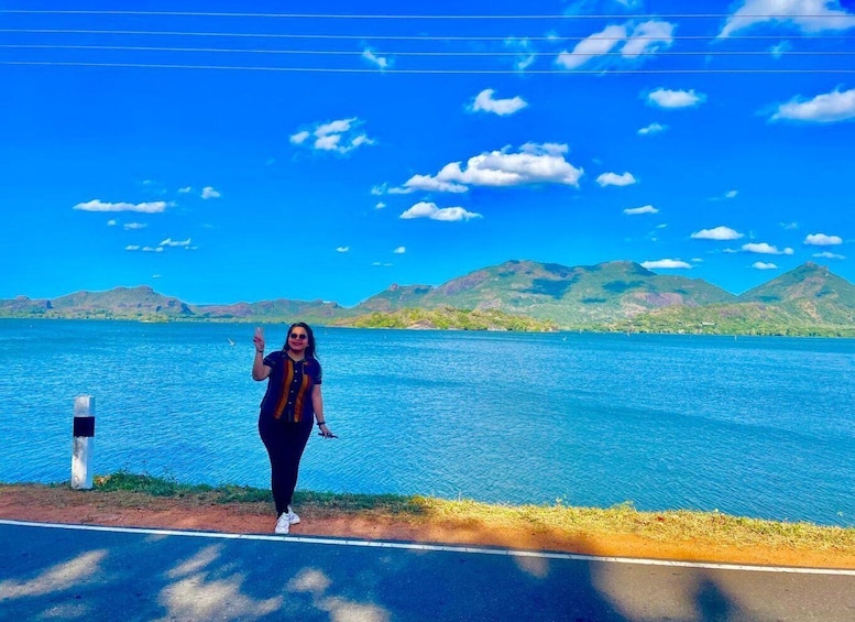 A person standing by a road with a lake and mountains in the background. 5