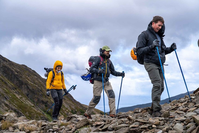 Three hikers on a rocky mountain trail with a cloudy sky. 3