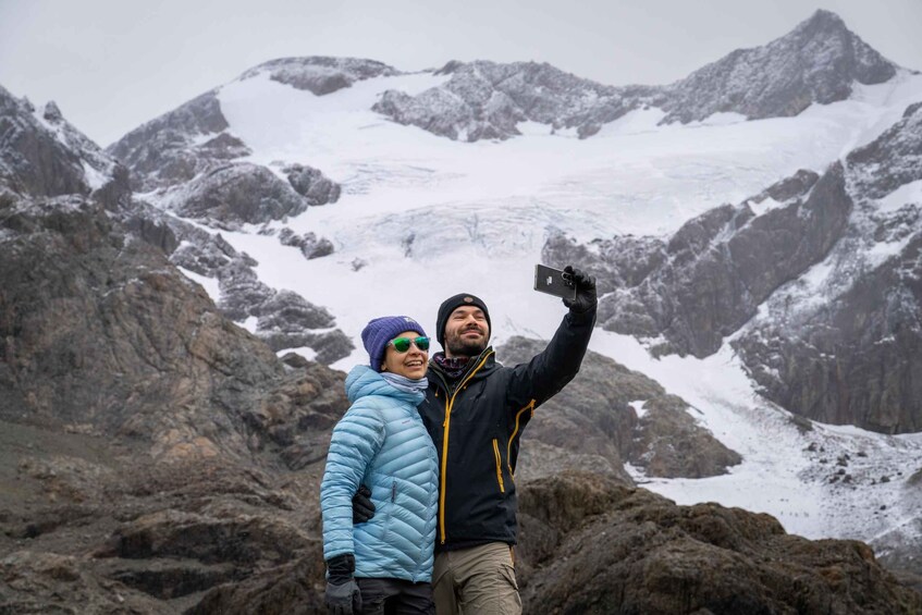 Two people taking a selfie with a glacier and mountains in the background. 1