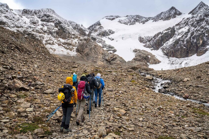 A group of hikers on a rocky mountain trail with snow-capped peaks in the background. 2