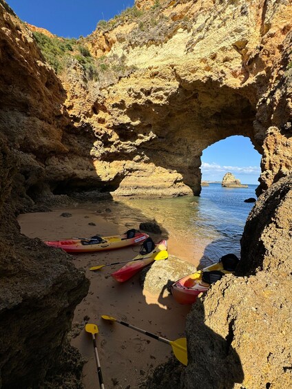 Kayaks on a sandy beach with a rocky archway. 3