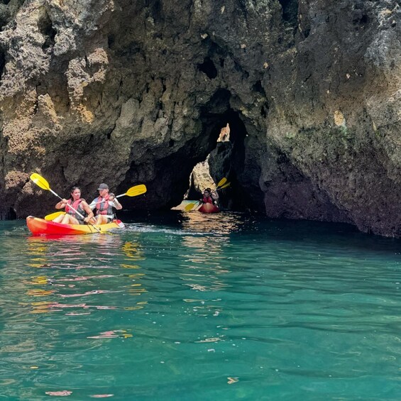Two people kayaking in a cove with a cave entrance in the background. 4