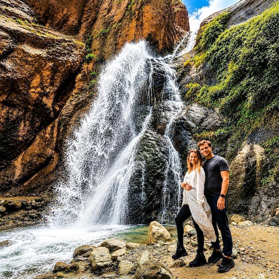 A waterfall, rocky terrain, and a couple standing in front of it. 4
