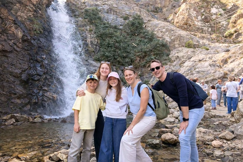 A group of people posing in front of a waterfall with rocky terrain and a clear stream. 5