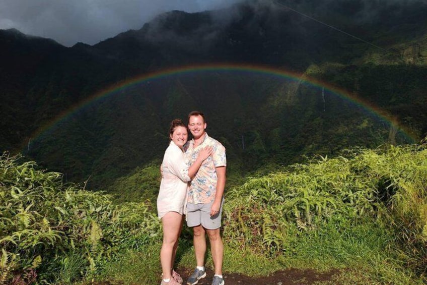 A couple standing with a rainbow in a mountainous area. 5