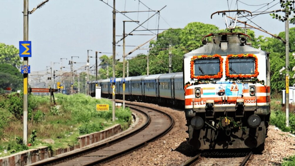 A train on tracks with overhead lines, surrounded by greenery and railway infrastructure. 2