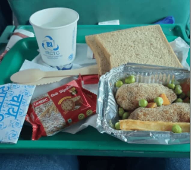 A meal tray with a sandwich, a cup, a packet of biscuits, a packet of peas, and a foil container with meatballs and peas. 4