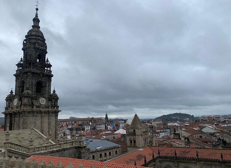 A historic tower with intricate architecture and a clock, surrounded by a cityscape with red-tiled roofs. 5
