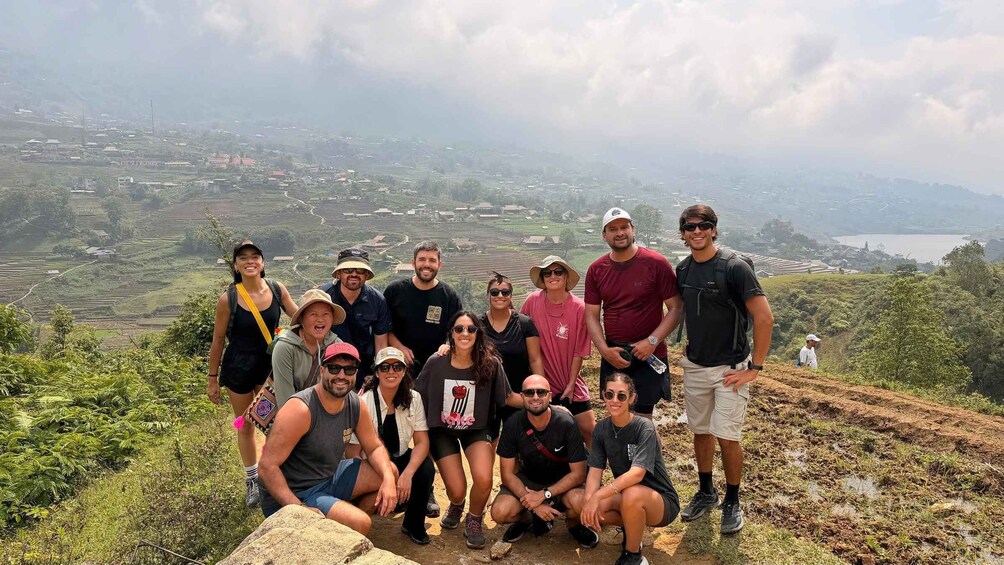 A group of people on a mountain trail with terraced fields and a lake in the distance. 2