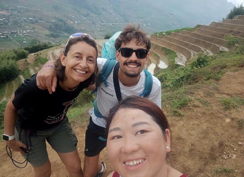 Three people on a hiking trail with terraced fields in the background. 4