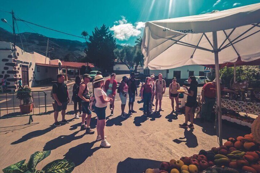 Un groupe de personnes se tient sous une tente, sur un marché où des fruits et des légumes sont exposés. 5