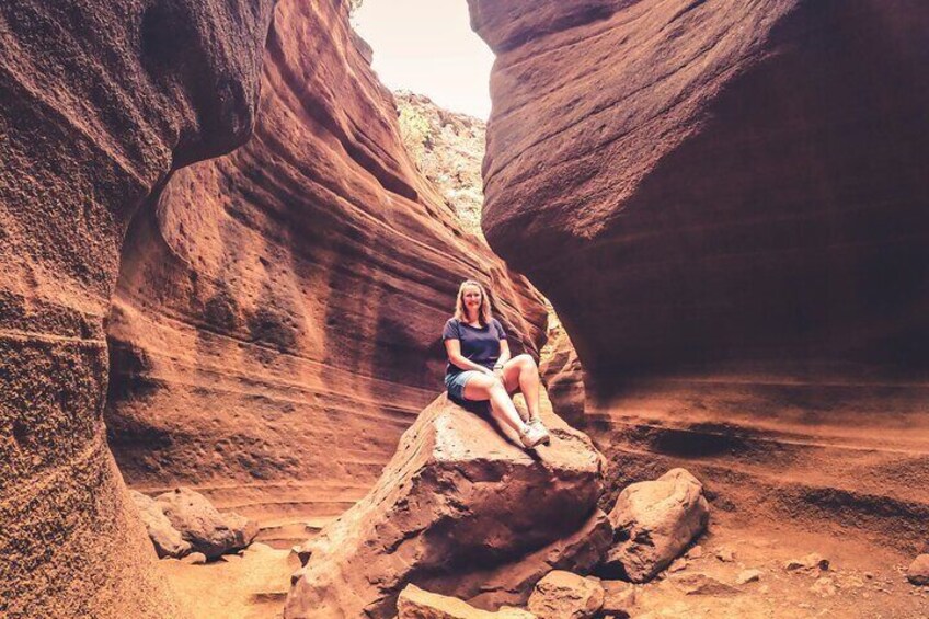A person sitting on a rock in a narrow canyon with red rock walls. 4