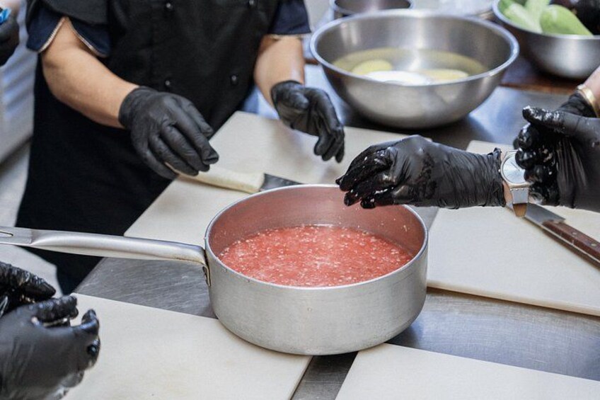 A person wearing black gloves handling a pot of red liquid, likely cooking or preparing food. 3