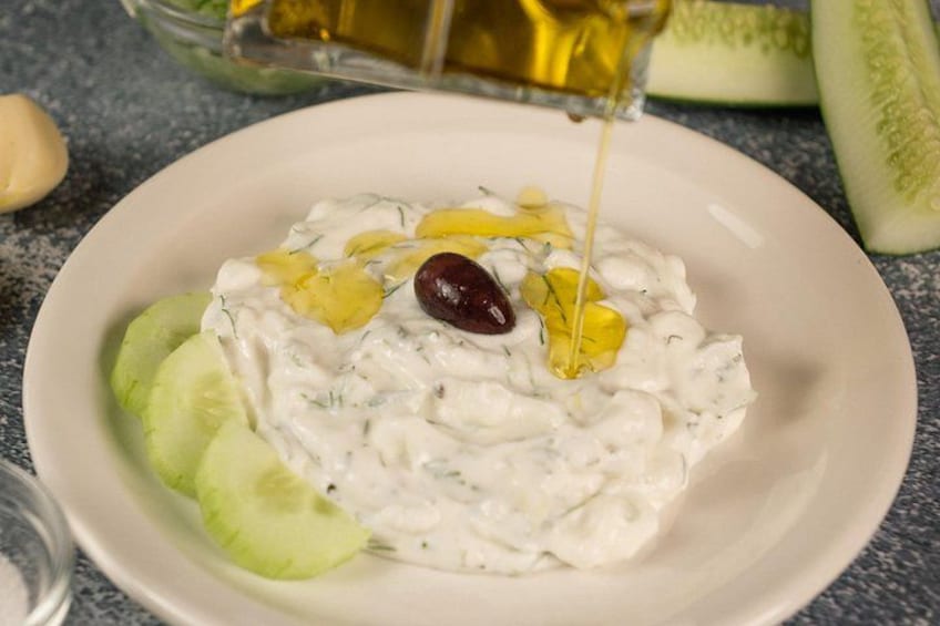 A bowl of tzatziki sauce with cucumber slices and a red olive on a plate. 4