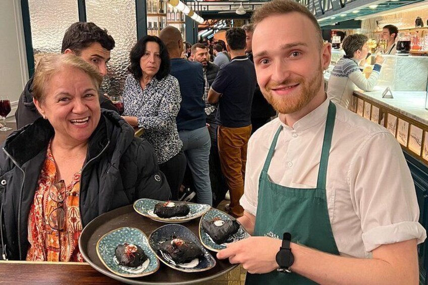En person som bär ett bricka med mat, en restauranginteriör och andra gäster i bakgrunden. 4