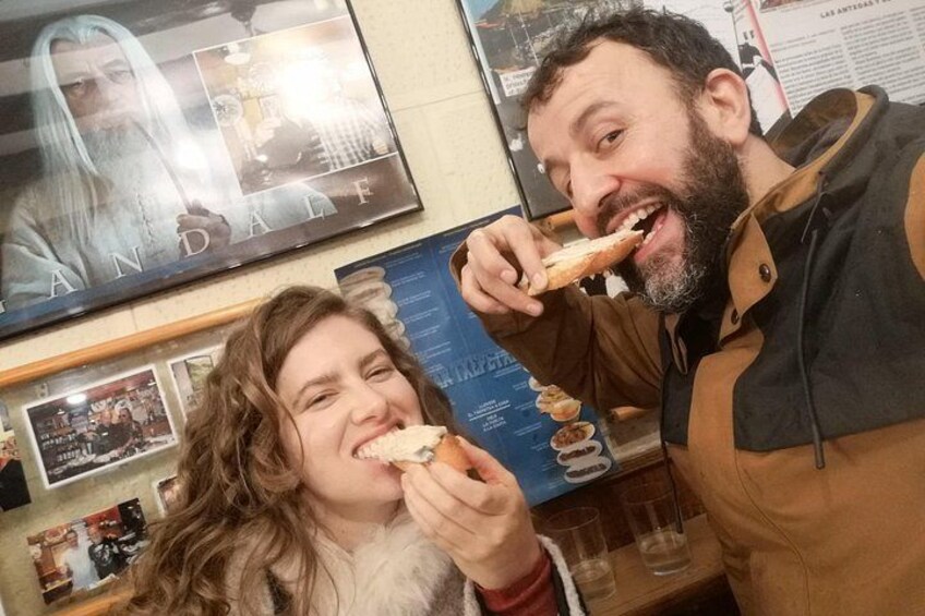Deux personnes sont assises dans un restaurant, en train de manger une pizza, avec un panneau affichant le menu en arrière-plan. 3