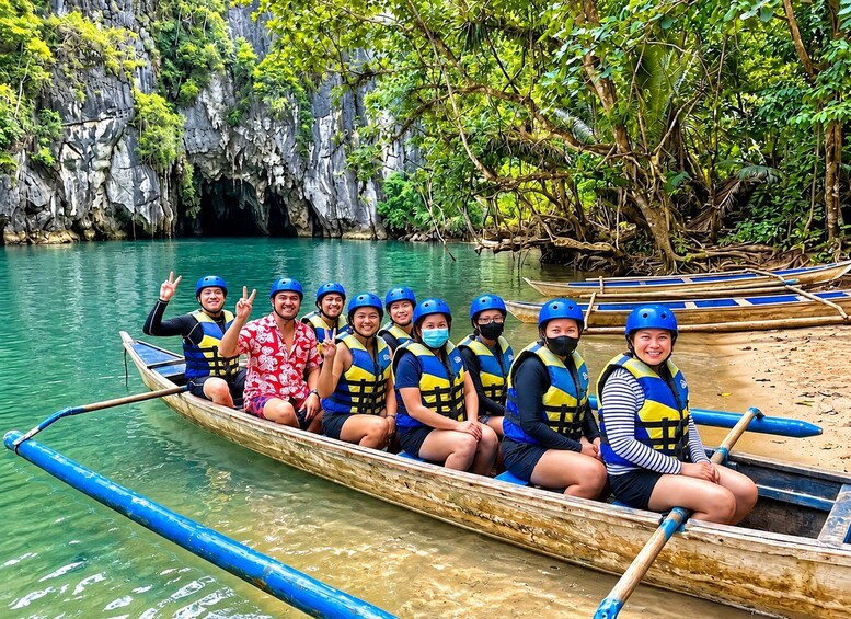 A group of people in a long wooden boat on a river, wearing life jackets and helmets, surrounded by greenery and rocky cliffs. 3