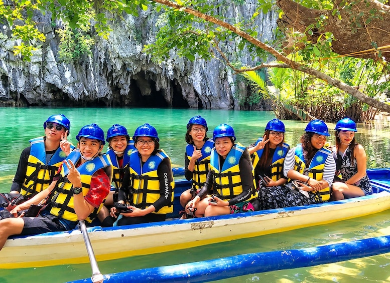 A group of people in a yellow and blue canoe on a river with a rocky cave backdrop. 5